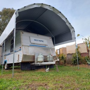 Large caravan shelter with an older caravan underneaet that reads Olympic on the back
