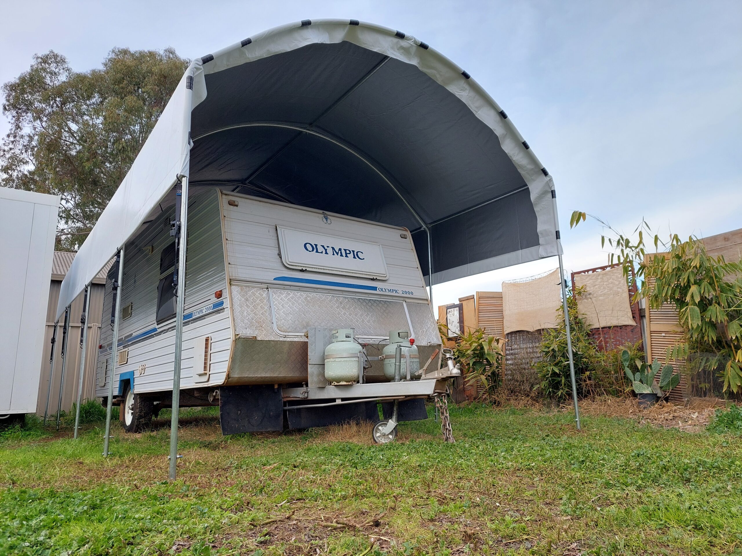 Large caravan shelter with an older caravan underneaet that reads Olympic on the back