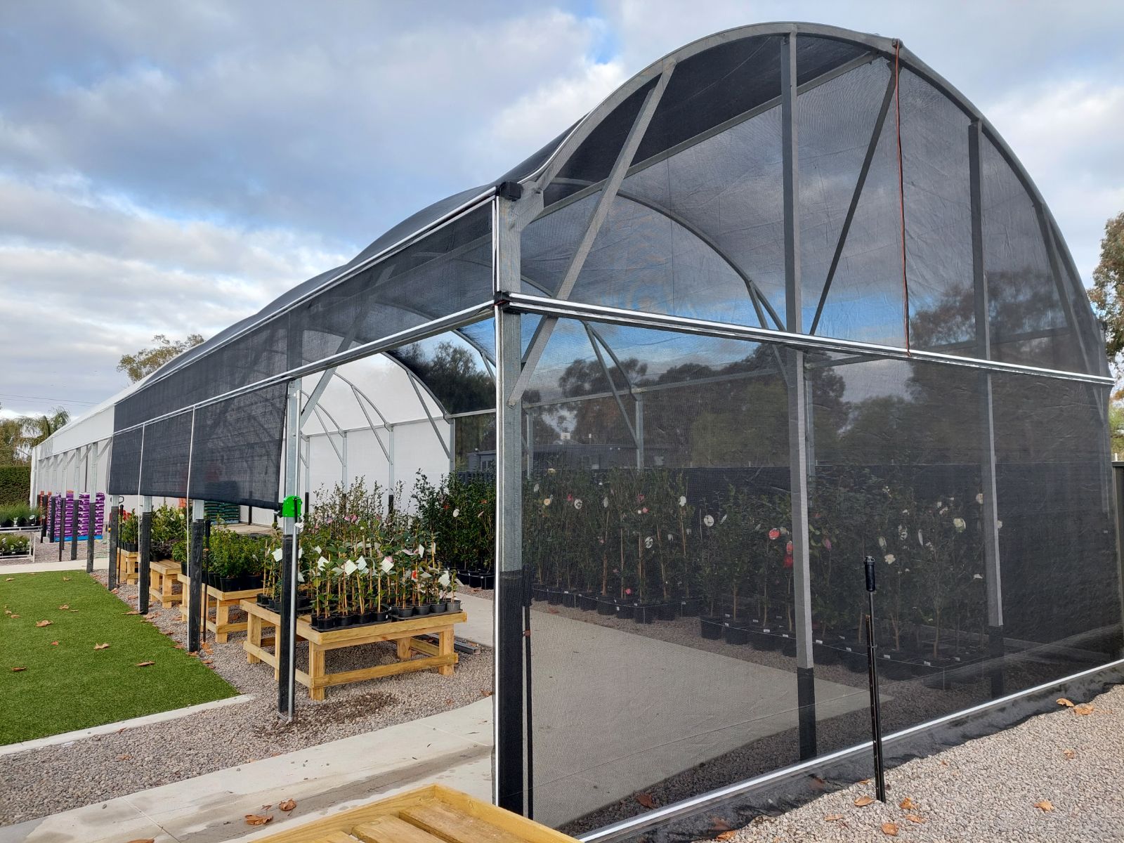 cloudy sky - arch greenhouse with dark netting - stands or plants growing underneath